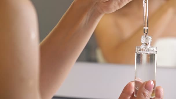 Kvinnlig hand håller ett kosmetiskt serum i en glasflaska med pipett. Reflektion i spegeln. Kosmetisk produkt för hudvård. — Stockvideo