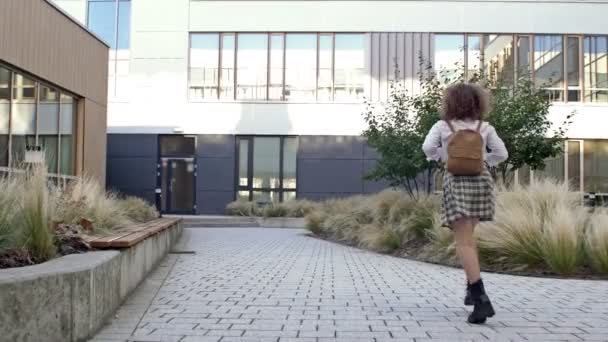 La studentessa è in ritardo per la scuola. Bella ragazza adolescente correre con uno zaino dietro la schiena sullo sfondo dell'edificio scolastico. Ritorno a scuola. — Video Stock