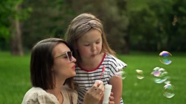 Genç bir kadın ve 6 yaşındaki kızı gökkuşağı sabun köpüğü üflüyorlar. Eğlenceli aile tatili..