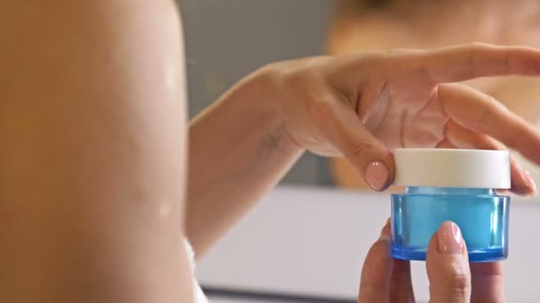 La mano delle donne tiene una crema idratante anti-invecchiamento in un barattolo di vetro blu. Riflessione nello specchio. Prodotto cosmetico per la cura della pelle. — Video Stock