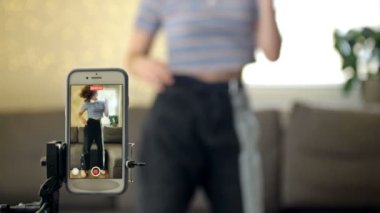 Neşeli genç kız kameranın önünde dans ediyor. Evde tripodla telefon çekiyor. Moda içeriğini sosyal medyada paylaşmak için mobil bir uygulama üzerinde yaratıyor..