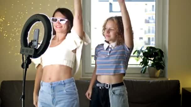 Veselá mladá žena a její dospívající dcera aktivně tancují, pohybují se emocionálně, baví se před kamerou, natáčejí video pomocí telefonu na stativu doma, vytvářejí si vlastní — Stock video