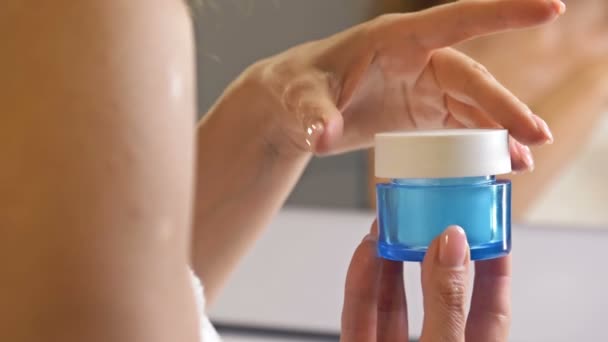 Женская рука держит антивозрастной увлажнитель в синей стеклянной банке. Отражение в зеркале. Косметический продукт по уходу за кожей. — стоковое видео
