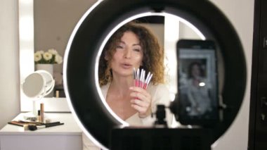 Güzel, orta yaşlı güzellik blogcusu dudak kalemi hakkında konuşuyor. Aynanın karşısında oturan ve kameranın yansıttığı bir kadın. 4K.