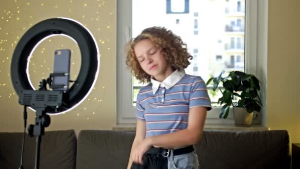 Allegro teenager che balla davanti alla telecamera filmando video usando il telefono su treppiede a casa, creando i suoi contenuti di tendenza su un'app mobile da condividere sui social media. Tik Tok. — Video Stock
