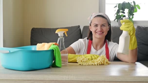 A fiatal, vidám háziasszony készen áll a takarításra. Egy takarítócég tisztítószerekkel körülvett alkalmazottja készen áll a munkára. Háztartási munka fogalma. — Stock videók