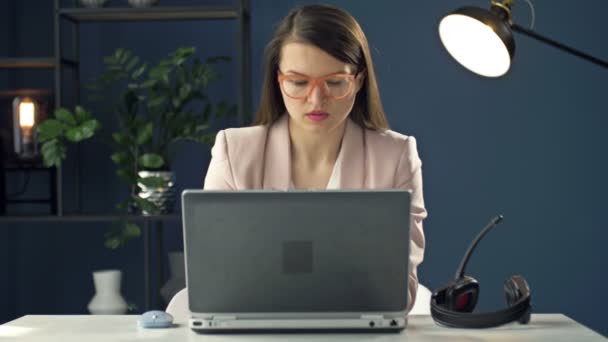 Retrato de uma jovem mulher em um fone de ouvido trabalhando em um laptop. Operador de call center educado. Mulher de negócios se comunica com um sorriso com parceiros de negócios. — Vídeo de Stock