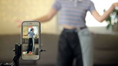 Neşeli genç kız kameranın önünde dans ediyor. Evde tripodla telefon çekiyor. Moda içeriğini sosyal medyada paylaşmak için mobil bir uygulama üzerinde yaratıyor..