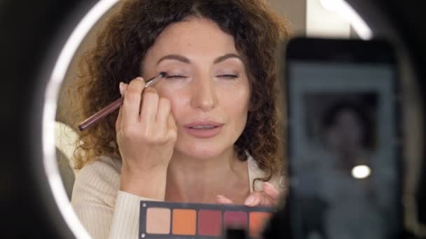 La blogueuse beauté bien soignée d'âge moyen parle du maquillage des yeux. Une femme assise devant un miroir et une caméra vidéo. — Video