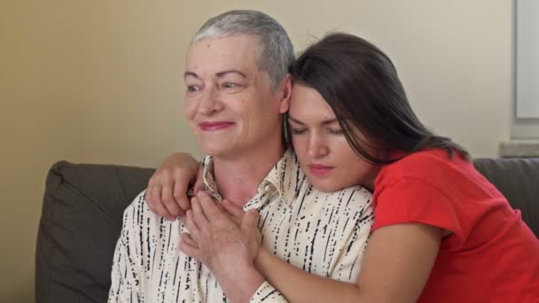 Een volwassen dochter knuffelt haar moeder. Een oudere vrouw heeft haargroei na chemotherapie. Liefde, zorg en ondersteuning in de familie van een kankerpatiënt. — Stockvideo