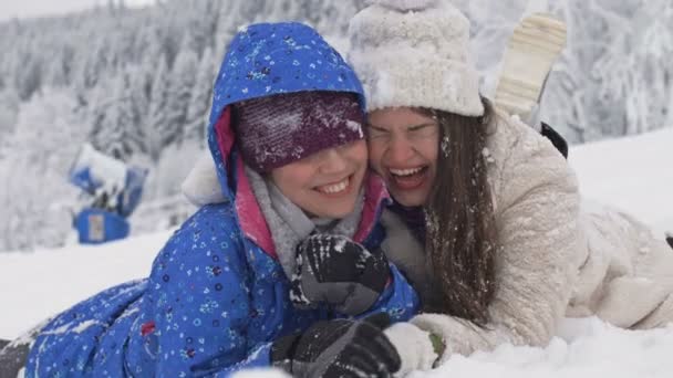 Zwei junge Frauen liegen im Schnee und lachen. Winterspaß. — Stockvideo