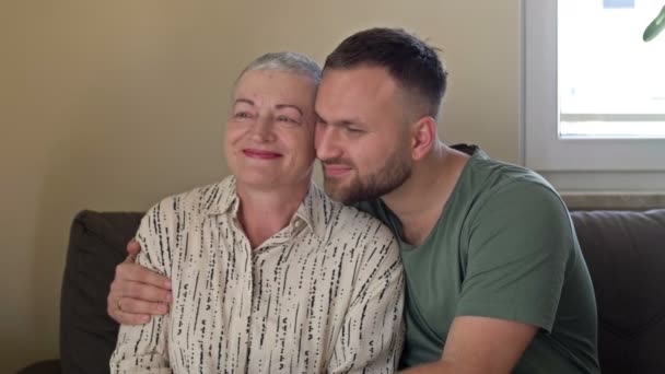 Een volwassen zoon knuffelt zijn moeder. Een oudere vrouw heeft hergroei van haar na chemotherapie. Liefde, zorg en ondersteuning in de familie van een kankerpatiënt. — Stockvideo