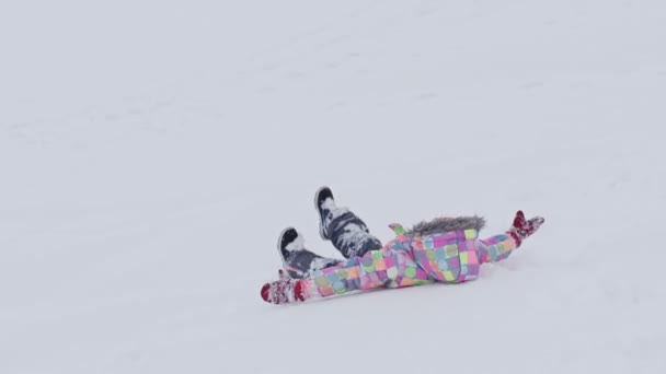 Veselá sedmiletá dívka v zimním oblečení leží na sněhu a dělá anděla ve sněhu. Dítě je šťastné.. — Stock video