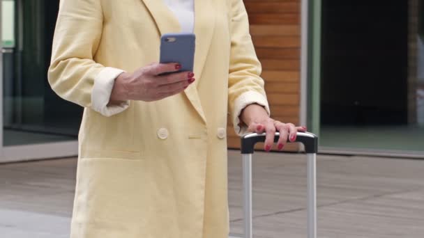 Bavullu bir iş kadını cep telefonu kullanıyor ve birini bekliyor.. — Stok video