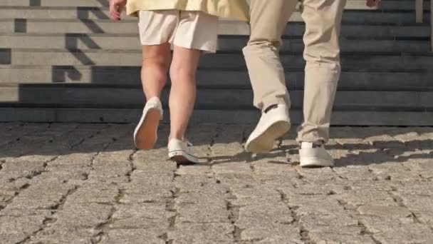 Pieds masculins et féminins montant les escaliers dans des chaussures décontractées confortables. Couple d'âge mûr monte facilement les marches d'un escalier en pierre. Vue arrière. — Video