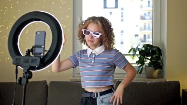 Menina adolescente alegre dançando na câmera filmando vídeo usando telefone no tripé em casa, criando seu conteúdo na moda em um aplicativo móvel para compartilhar nas mídias sociais. — Vídeo de Stock