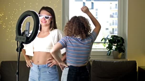 Veselá mladá žena a její dospívající dcera aktivně tancují, pohybují se emocionálně, baví se před kamerou, natáčejí video pomocí telefonu na stativu doma, vytvářejí si vlastní — Stock video