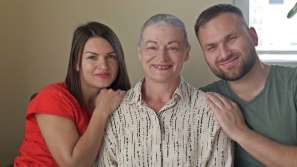 Familie portret. Volwassen zoon en dochter knuffelen een oudere moeder. Vrouw na chemotherapie en de kinderen ondersteunen de moeder. Gezinswaarden. — Stockvideo