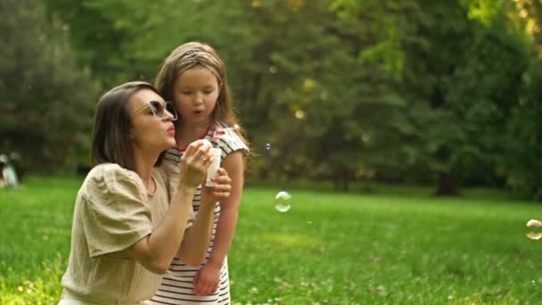 Jeune femme et sa fille de 6 ans soufflent des bulles de savon arc-en-ciel. Vacances amusantes en famille. — Video
