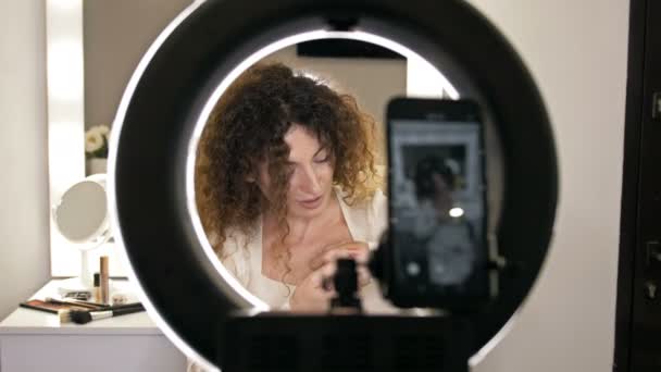 Красивий блогер краси середнього віку розповідає про лайнери для губ. Жінка сидить перед дзеркалом, в якому відображається відеокамера . — стокове відео