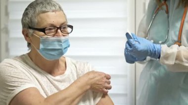 Yaşlı bir kadının koronavirüse karşı aşılanması. Bir kadın doktor ya da hemşire hastaya bir sonraki aşıyı yapar..