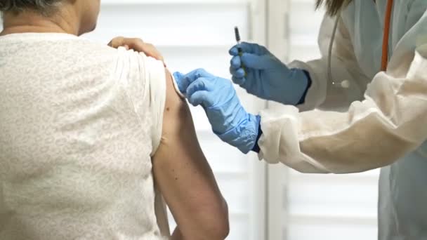 Вакцинация пожилой женщины против коронавируса. Женщина-врач или медсестра назначает пациенту следующую дозу вакцины. — стоковое видео