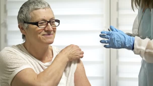 Vaccinatie van een oudere vrouw tegen het coronavirus. Een vrouwelijke arts of verpleegkundige dient de volgende dosis vaccin toe aan de patiënt. — Stockvideo