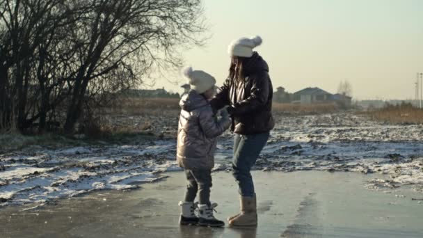 Young woman with a daughter of 7-8 years old glide merrily on the ice of a frozen lake. Both fall and laugh. — Stockvideo