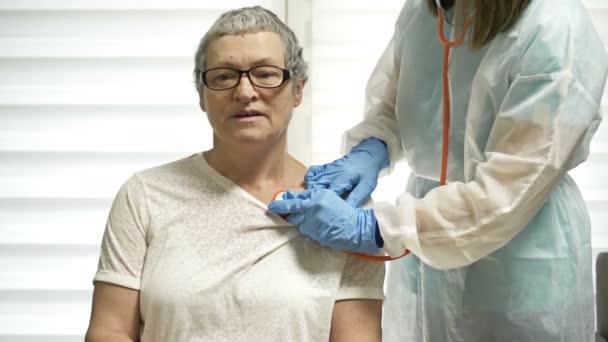 Kadın doktor, koronavirüs belirtileri gösteren yaşlı bir hastayı fonendoskopla dinliyor.. — Stok video