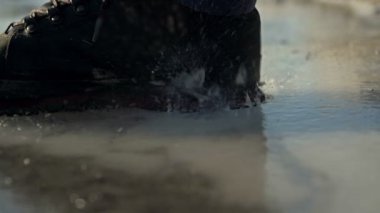 Siyah çizmedeki insan bacağı donmuş bir su deposunun buzlu yüzeyine çarpar..