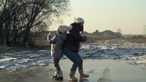 Young woman with her daughter 7-8 years old glide cheerfully on the ice of a frozen lake. They are trying to dance. — Vídeo de Stock