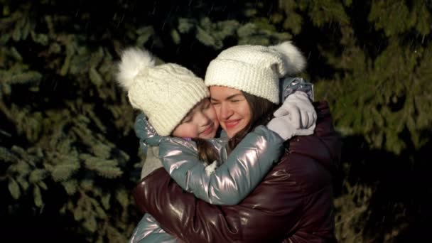 Young woman and a girl of 7-8 years old tenderly hug each other. Mom m daughter on a walk in the winter forest. Family holiday. — Stock videók