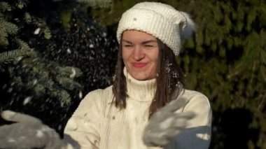 Hafif giysili neşeli genç kadın ilk karda seviniyor ve ormanda oynuyor..