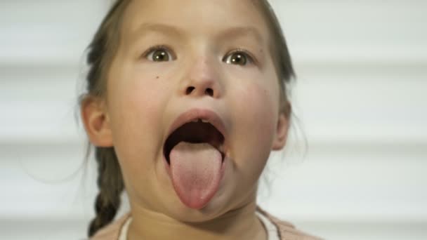 Niña de 7-8 años muestra diligentemente su lengua. Tal vez en una cita con un médico. — Vídeo de stock