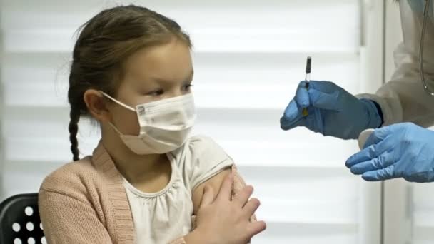Enfermeira em um uniforme de proteção e uma máscara médica dá uma injeção da vacina covid-19 para uma menina de 7-8 anos de idade. Vacinação de crianças. — Vídeo de Stock