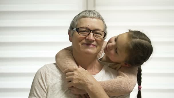 A 7-8 year old girl affectionately hugs her elderly grandmother. Grandma is happy. Family values. — Stockvideo