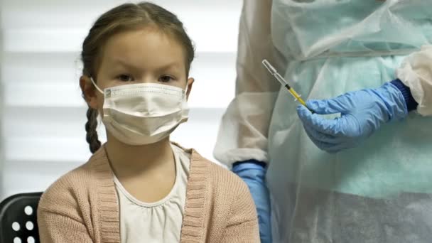 Krankenschwester in Schutzuniform und medizinischer Maske gibt einem 7-8-jährigen Mädchen eine Injektion des Covid-19-Impfstoffs. Impfung von Kindern. — Stockvideo