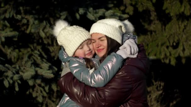 Jonge vrouw en een meisje van 7-8 jaar oud knuffelen elkaar teder. Mam en dochter op een wandeling in het winterbos. Gezinsvakantie. — Stockvideo