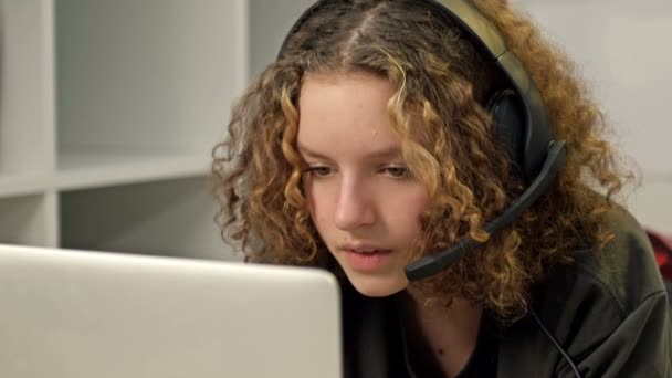 Smiling teenage girl using laptop and wearing headphones. Modern technologies and the concept of leisure, education and communication. — ストック動画