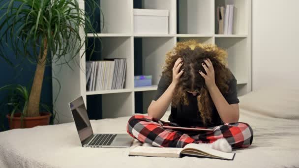 Dificultades de la enseñanza a distancia. Adolescente haciendo deberes sentada en la cama en casa. No todo funciona, la chica está molesta.. — Vídeo de stock