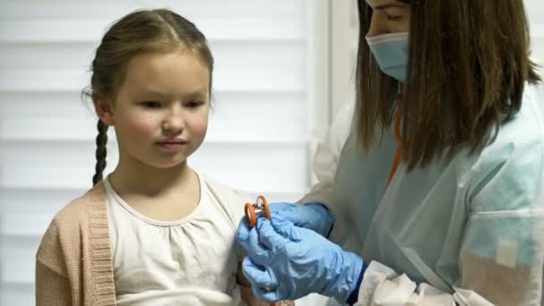 Female doctor listens with a phonendoscope to a girl patient 7-8 years old patient. Pediatrics. — Stock Video