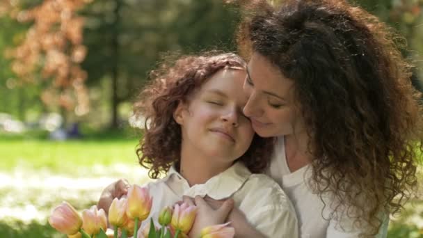 Портрет женщины, обнимающей свою дочь-подростка букетом тюльпанов. На фоне весенней природы. День матери. — стоковое видео