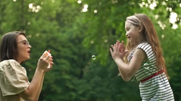 Jonge vrouw blaast zeepbellen. Haar 6-jarige dochter vangt graag regenboogbubbels. Gezinsvakantie. — Stockvideo