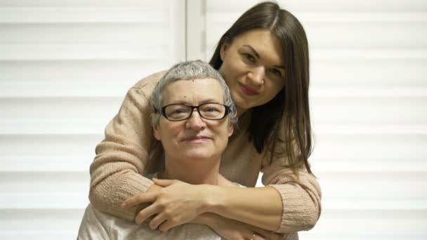 Взрослая дочь обнимает свою мать. Пожилая женщина восстанавливает волосы после химиотерапии. Любовь, уход и поддержка в семье больного раком. — стоковое видео