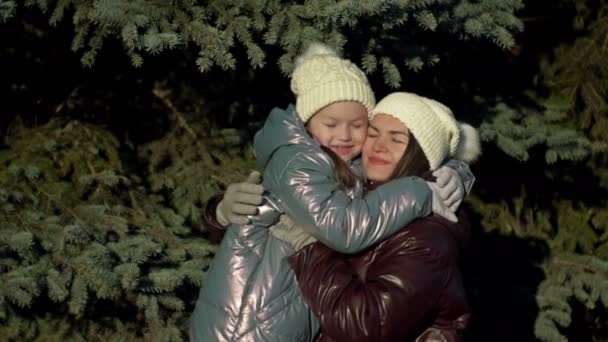 Walk in the winter forest. A girl of 7-8 years old gently hugs her mother. Young woman points out something interesting to her daughter. Family holiday. — Vídeo de Stock