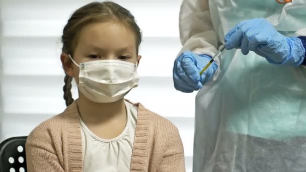 Enfermeira em um uniforme de proteção e uma máscara médica dá uma injeção da vacina covid-19 para uma menina de 7-8 anos de idade. Vacinação de crianças. — Vídeo de Stock