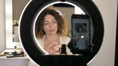 Neşeli kadın vlogger video kaydederken kozmetik ürünleri gösteriyor ve güzellik blogu için tavsiyelerde bulunuyor. El kremi.
