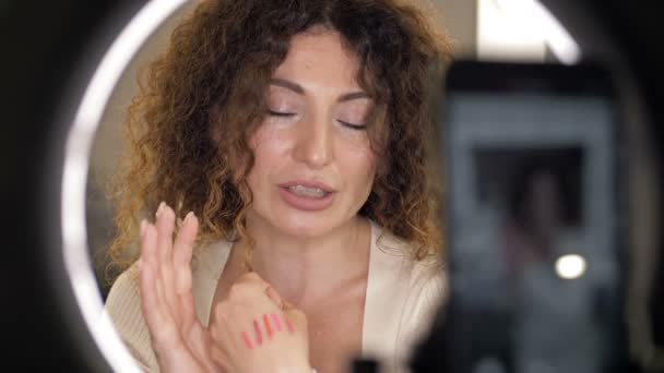 Vacker, medelålders skönhetsbloggare pratar om läppstift. Kvinna som sitter framför en spegel där en videokamera reflekteras. — Stockvideo
