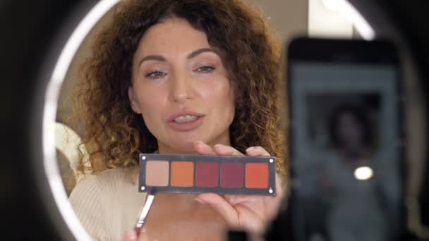 Mooie vrouw van middelbare leeftijd schoonheid blogger praat over oogschaduwen en oogmake-up. Vrouw zit voor een videocamera. — Stockvideo