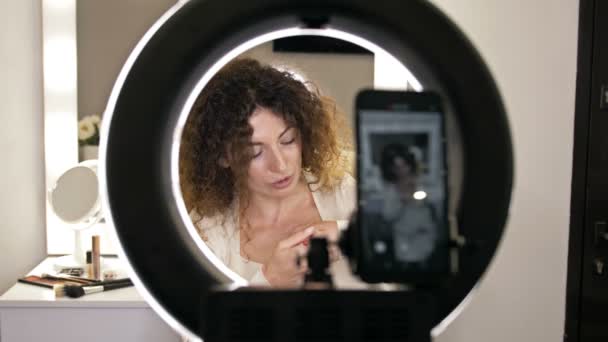 Beautiful, middle-aged beauty blogger talks about lip liners. Woman sitting in front of a mirror in which a video camera is reflected. — Stock Video